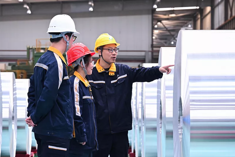 Técnicos inspeccionando bobinas de aluminio terminadas en el área de producción de la fábrica.