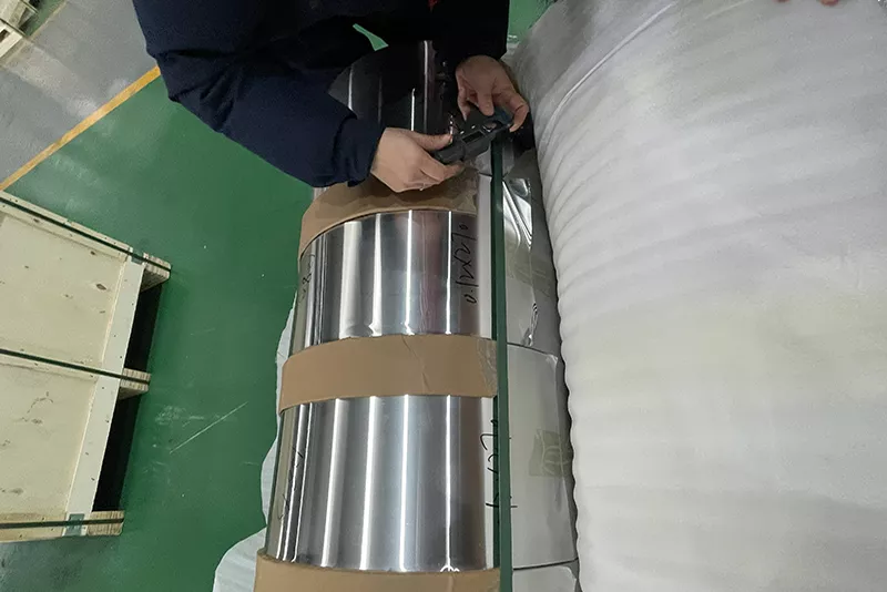 Inspector verificando el estado del borde de la bobina de aluminio y la tolerancia de espesor.